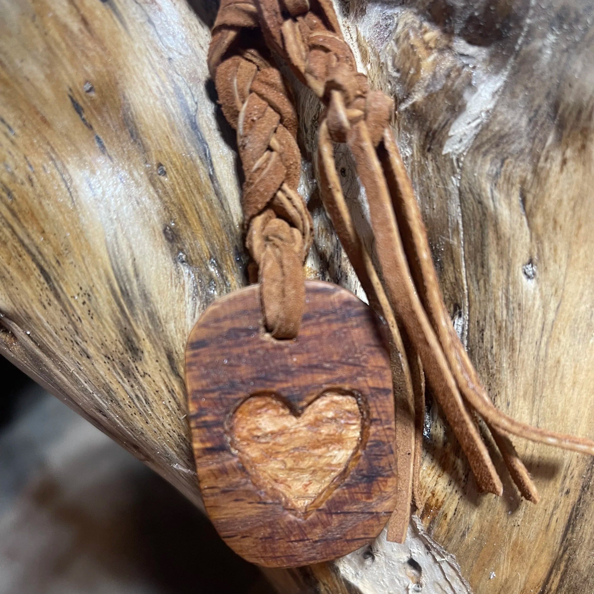 Wooden pendant with a heart cutout on a braided cord against a wooden background made by Little Valley Wood Shop